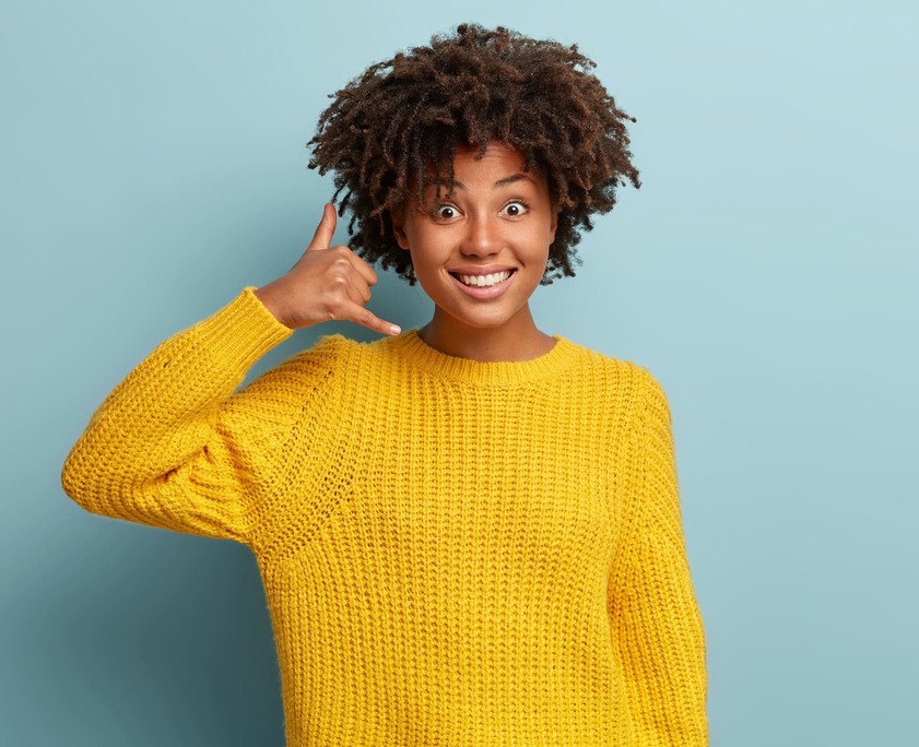 young-woman-with-afro-haircut-wearing-yellow-sweater miming a phone call